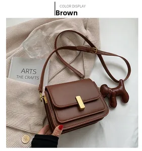 Detailed view of brown leather bag with gold rectangular buckle and cute dog charm