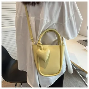 Vista dettagliata della borsa a secchiello gialla con ciondolo a cuore indossata dal modello