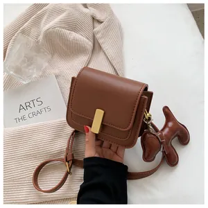 Detail view of brown leather crossbody bag with gold metal buckle and puppy charm