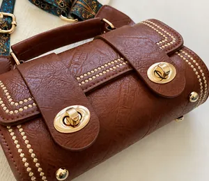 Detailed shot of brown textured leather bag with dual gold locks and ethnic strap