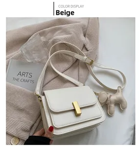 Detail of beige rectangular crossbody bag with golden clasp and cute puppy charm accessory