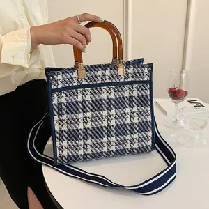 Detail of blue plaid tweed tote bag featuring amber resin handle and striped strap