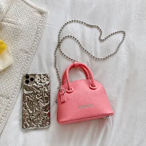 Mini borsa rosa con trama litchi accanto a uno smartphone per mostrare la taglia compatta