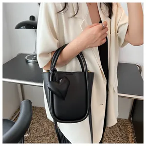 Dettaglio di una borsa a secchiello nera in pelle con ciondolo a cuore su una modella