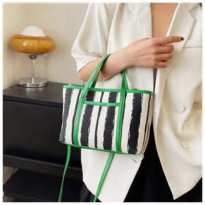 Dettaglio della borsa tote in tela a righe con finiture in pelle verde e tracolla