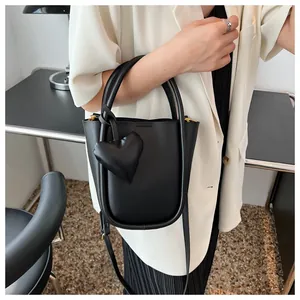 Dettaglio di una borsa a secchiello in pelle nera con ciondolo a cuore e tracolla regolabile