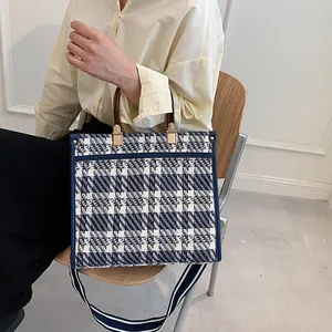 Detail of blue and white tweed tote bag with wooden handles and striped strap
