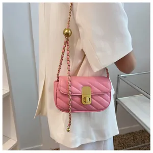 Sac bandoulière matelassé rose avec chaîne dorée porté sur un blazer blanc chic