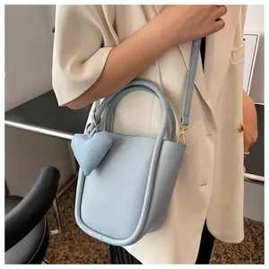 Dettaglio della borsa a secchiello azzurra con ciondolo a cuore e tracolla sottile sul modello