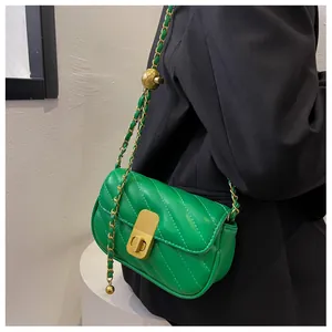 Détail du sac matelassé vert avec chaîne à boule dorée sur un tailleur noir élégant