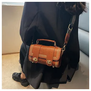 Detail of a brown textured crossbody bag with double gold twist locks and studded edges