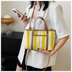Dettaglio di una borsa tote a righe con manici in pelle su un blazer bianco raffinato
