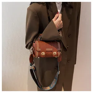 Detail of a brown leather crossbody bag with white stitching and geometric print strap