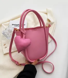 Borsa a secchiello rosa con ciondolo a cuore e tracolla su sfondo minimalista elegante