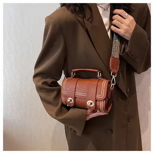 Detailed shot of a brown vintage cylinder crossbody bag with golden studs and wide strap
