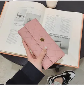 Portafoglio lungo rosa trapuntato con fibbia a camelia dorata su sfondo di un libro