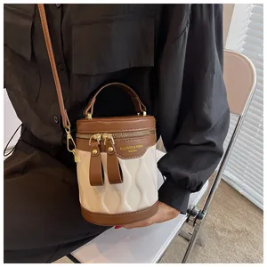 Detail of the wave-quilted cream bucket bag with brown trim and gold logo on the flap
