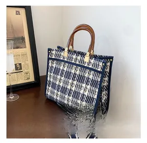 Detail of blue and white tweed tote bag with resin handles and striped strap on wood desk