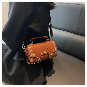 Detail of vintage brown crossbody bag with gold rivets and leather texture worn on black coat
