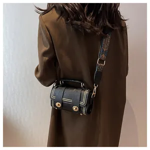 Detail of a black vintage cylinder bag with gold rivets and a colorful woven shoulder strap