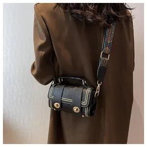 Close-up of black crossbody bag with gold studs and ethnic jacquard strap on a model