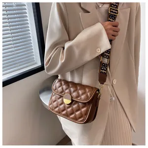 Detail of a brown quilted crossbody bag with a vintage gold lock and wide lettered strap