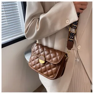 Detail of brown quilted crossbody bag with a round metal lock and jacquard strap