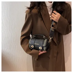 Detail of black crossbody bag with gold studs and colorful jacquard strap on a model