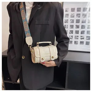 Close-up of off-white cylinder bag with decorative metal locks and ethnic woven strap