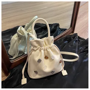 Detail einer beigen Beuteltasche mit Ziersteinen auf glattem schwarzem Seidenstoff