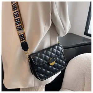 Detail of black quilted crossbody bag with gold lock and patterned wide strap