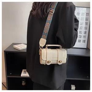 Detail of cream barrel crossbody bag featuring a jacquard strap and gold turn-lock
