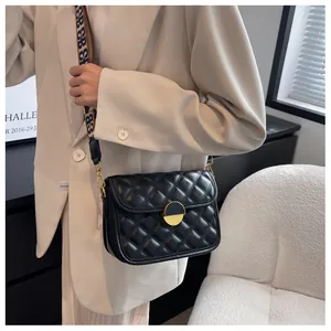Detail of black quilted crossbody bag with golden metal buckle and woven strap