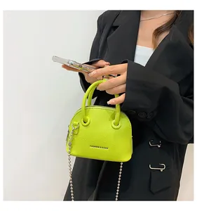 Dettaglio mini borsa verde neon in pelle martellata con catena argentata su blazer nero