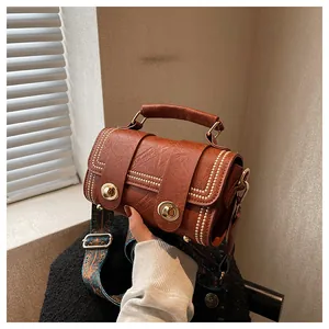 Detail of brown cylinder bag with gold rivets and bohemian strap held by hand