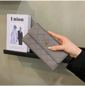 Portafoglio lungo grigio trapuntato con chiusura a fiore dorato, tenuto in mano da una modella