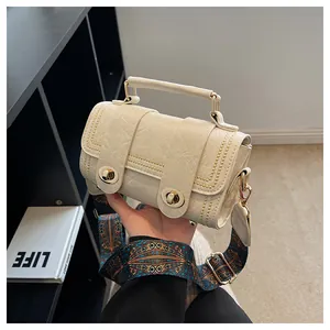 Detail of cream crossbody bag with gold stud trim and colorful ethnic pattern strap