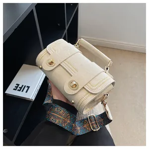 Detail of cream textured leather bag featuring gold twist locks and ethnic print strap