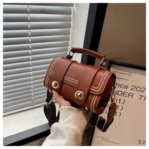 Detail of a brown leather bag featuring vintage rivets, metal locks, and a woven shoulder strap