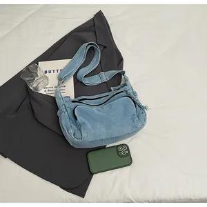 Flat lay of light blue denim messenger bag with multi-zipper pockets and shoulder strap