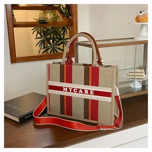 Dettaglio della borsa tote in tela a righe con tracolla rossa e motivo intrecciato