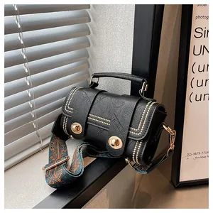 Detail of black crocodile embossed small square bag with golden studs and wide strap