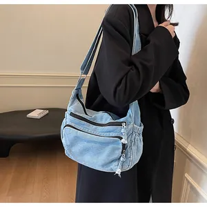 Detail of light blue denim messenger bag with multi-zipper pockets and utility strap