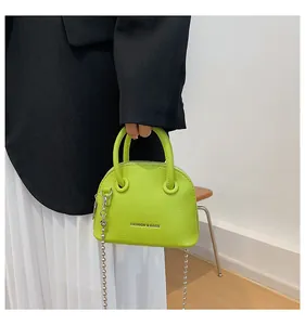 Mini borsa a conchiglia verde con trama litchi e catena argento indossata da modella