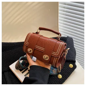 Close-up of vintage brown leather bag with golden rivets and woven geometric strap