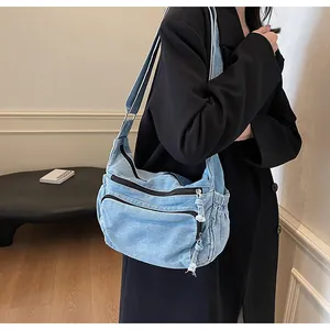 Close-up of light blue denim messenger bag with multiple functional zipper pockets