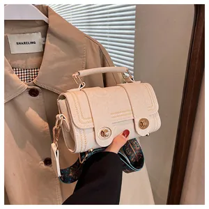 Detail of off-white textured crossbody bag featuring gold twist locks and vintage strap