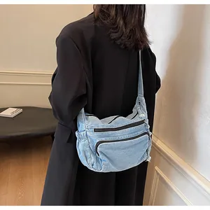 Detailed side view of washed light blue denim messenger bag on model with multiple pockets