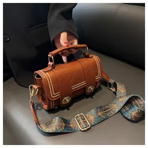 Close-up of brown leather bag featuring golden rivets and bohemian patterned wide strap