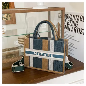 Dettaglio borsa tote in tela a righe con manici intrecciati e tracolla regolabile